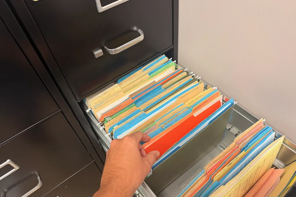 A hand reaching into an open drawer of color-coded file folders in a filing cabinet at the O'Malley Bail Bonds office